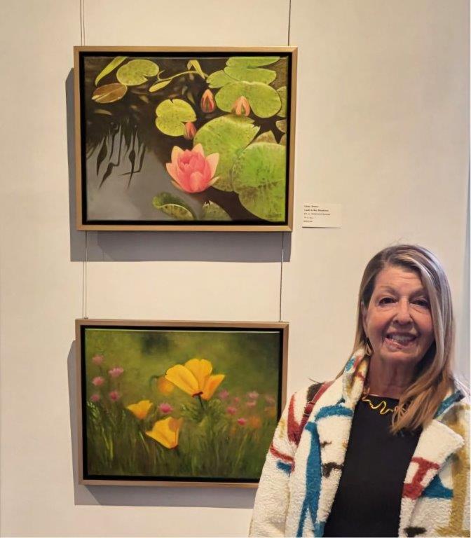Artist Helen Sklarz stands in an art gallery in front of her artwork hanging on the wall